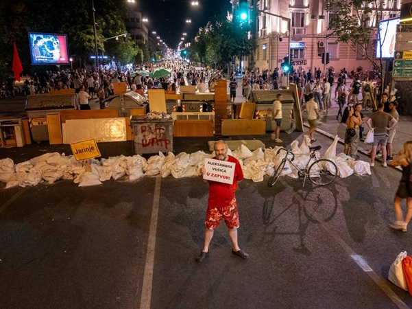 Street barricade with man holding a placard "Alexander Vucic to prison"