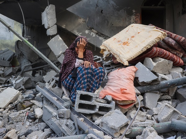 Woman in despair sitting amongst rubble of home in Gaza